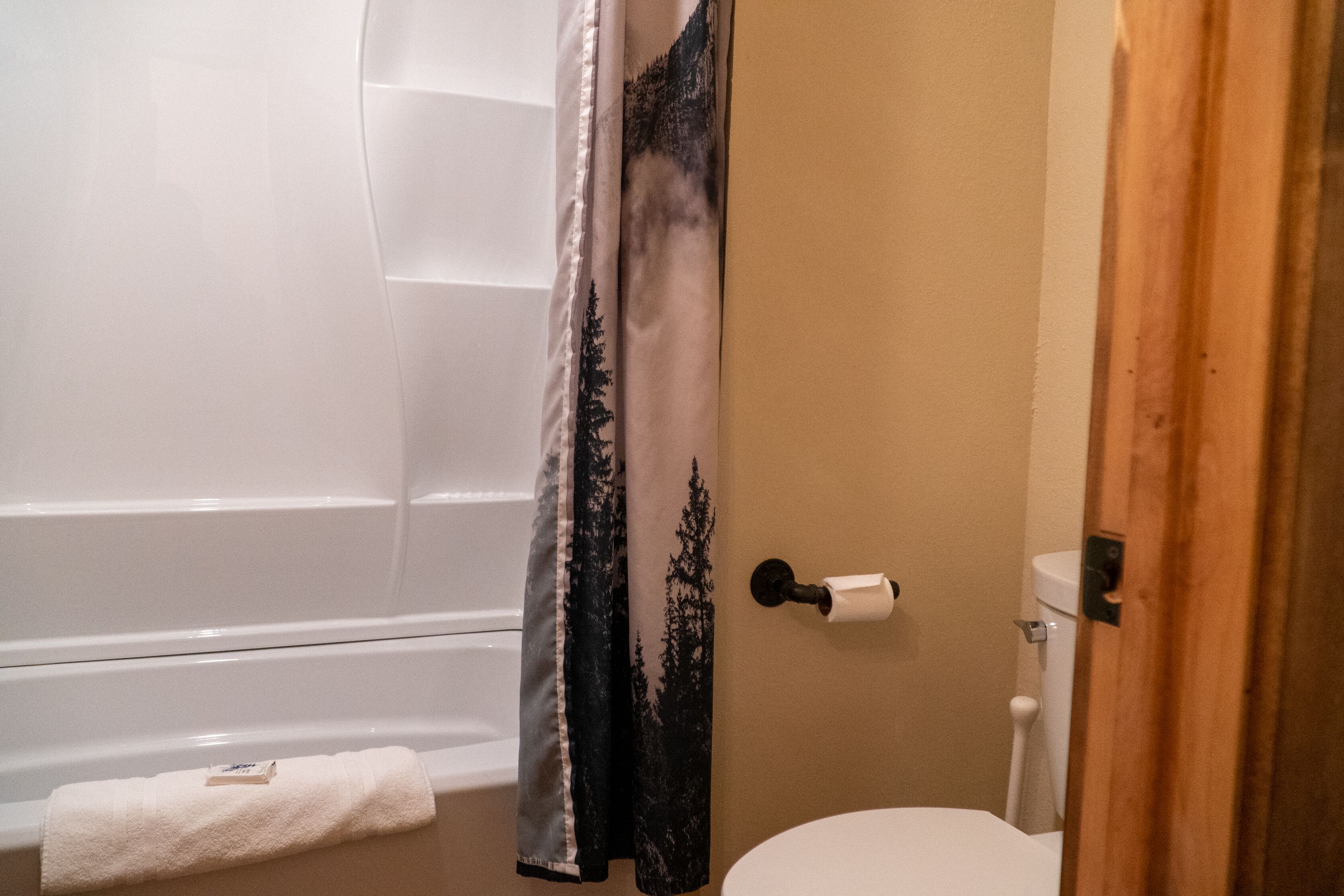 A bathroom with a bathtub, toilet, and a shower curtain with a forest design.