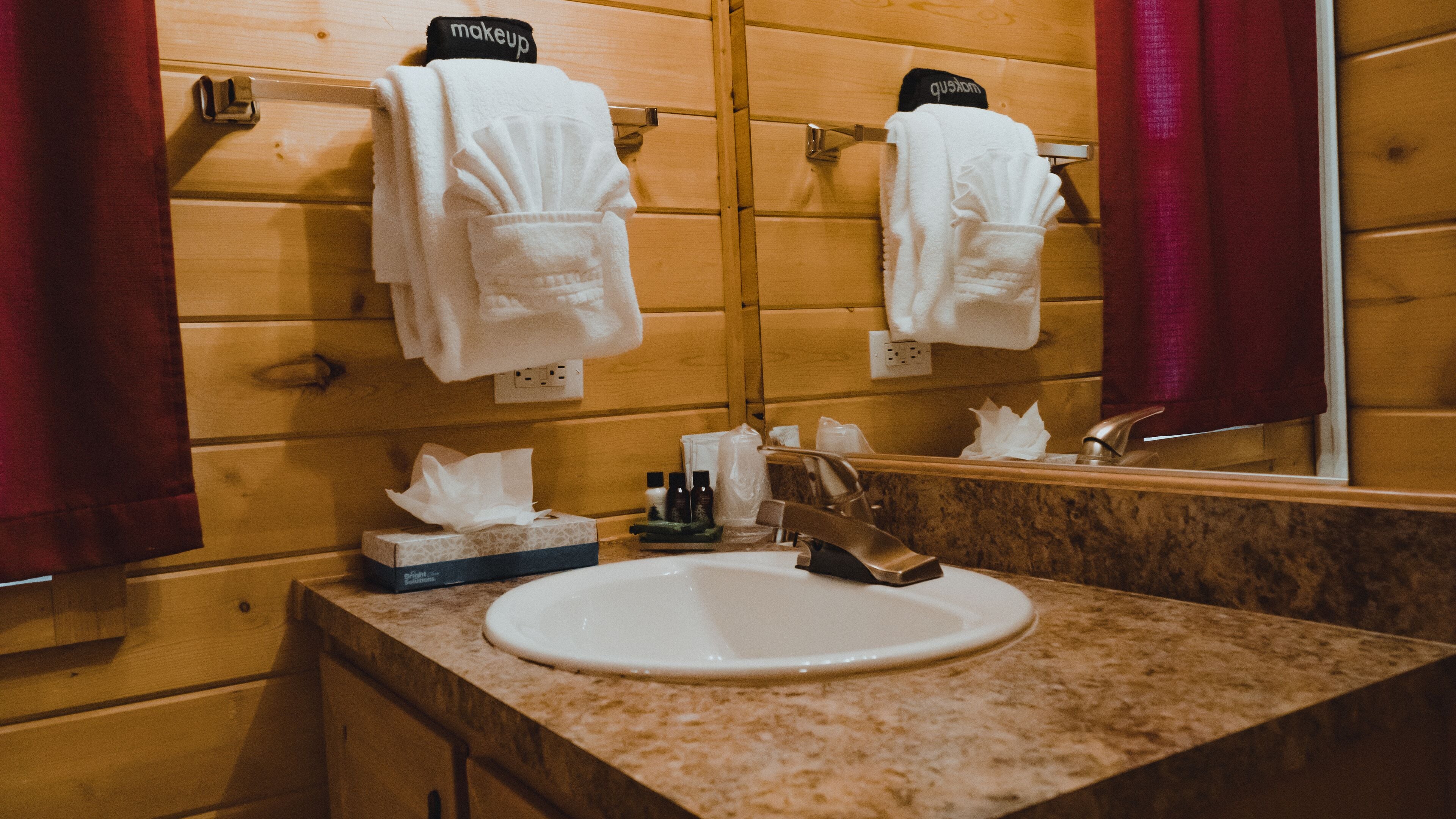 A bathroom with wooden panel walls, a sink with a marble countertop, and a mirror reflecting the towels.