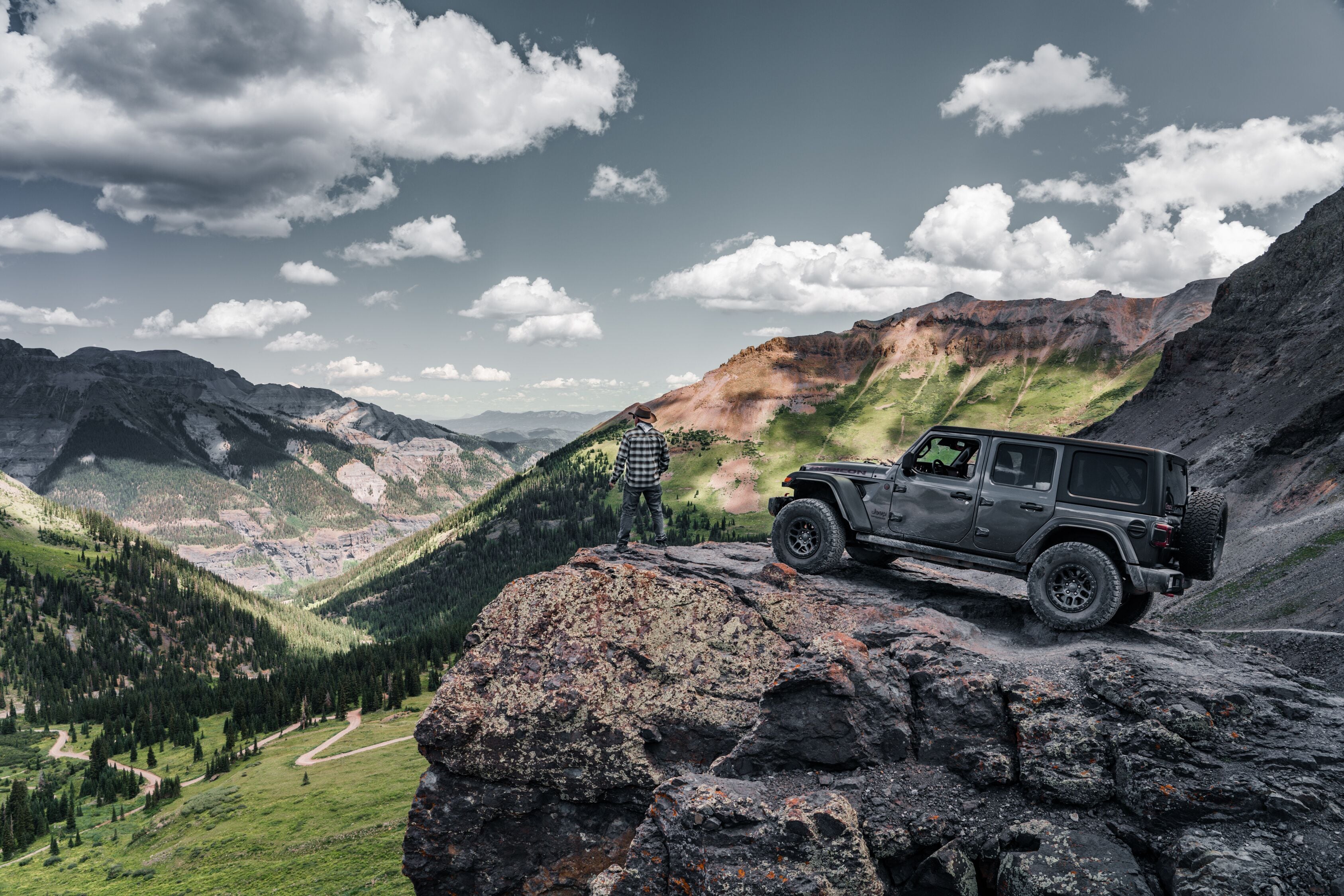 A rugged outdoor scene with a vehicle parked on a rocky outcrop overlooking a mountainous landscape.