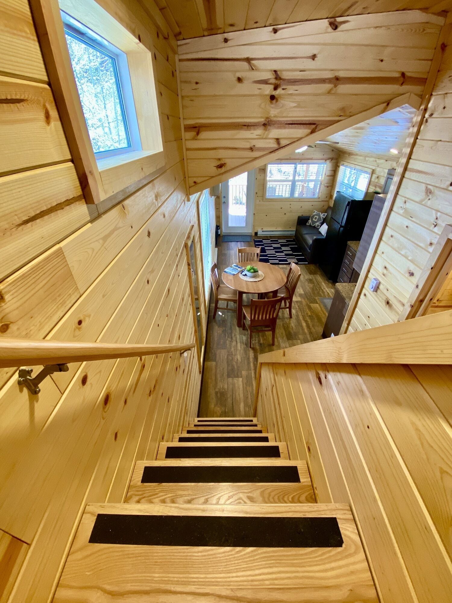 Interior de una cabaña de madera con una escalera central que lleva a un comedor y una sala de estar.