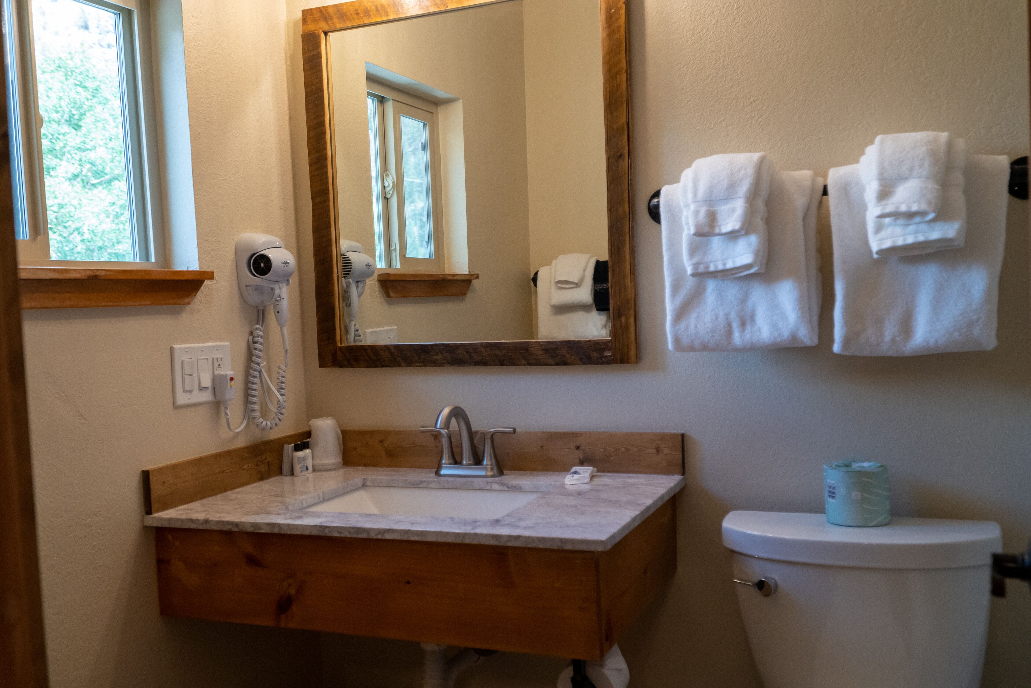 A bathroom with a wooden vanity, a sink, a mirror, a toilet, and a towel rack.