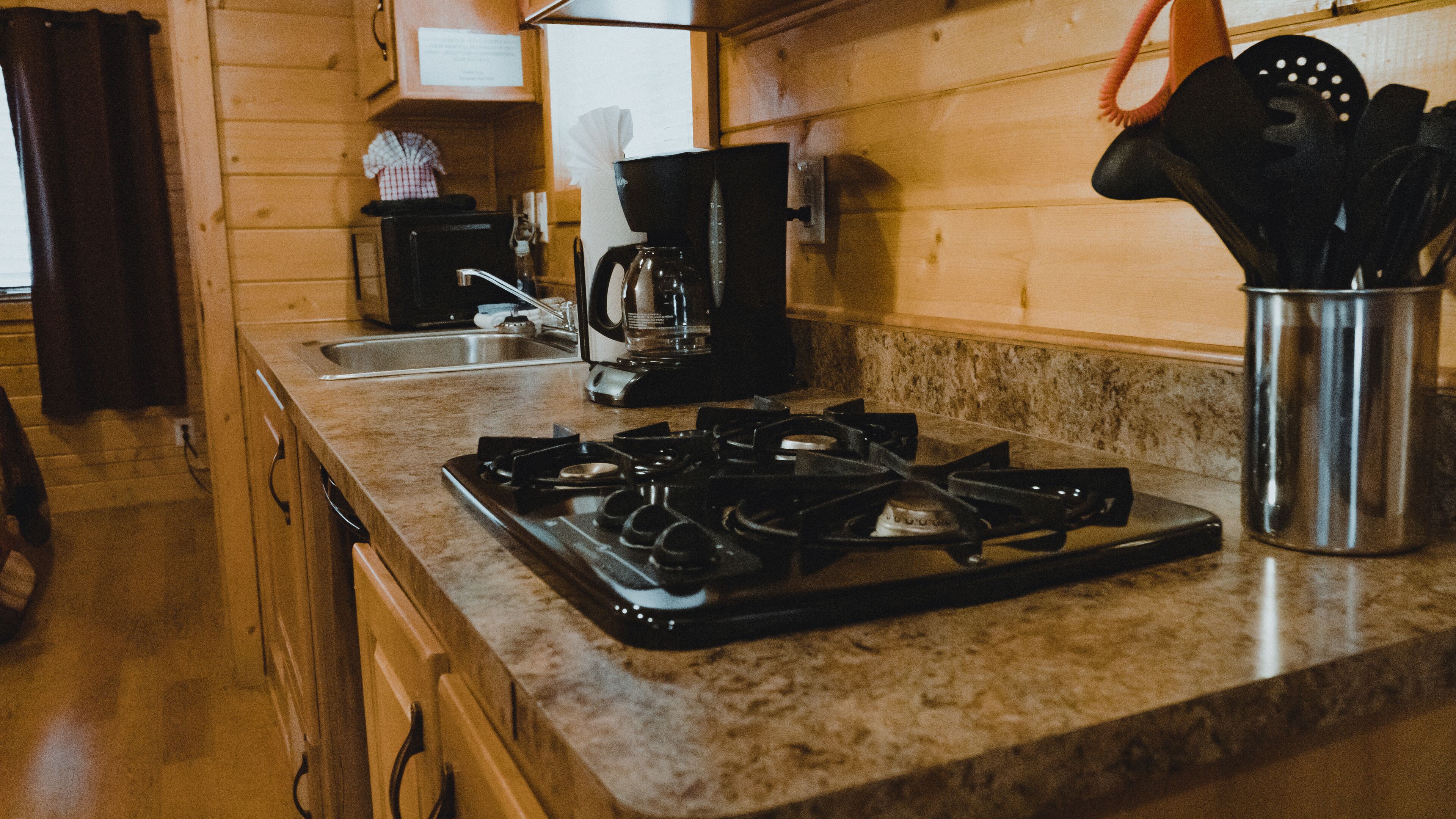 A kitchen with a gas stove, coffee maker, and utensils on the counter.