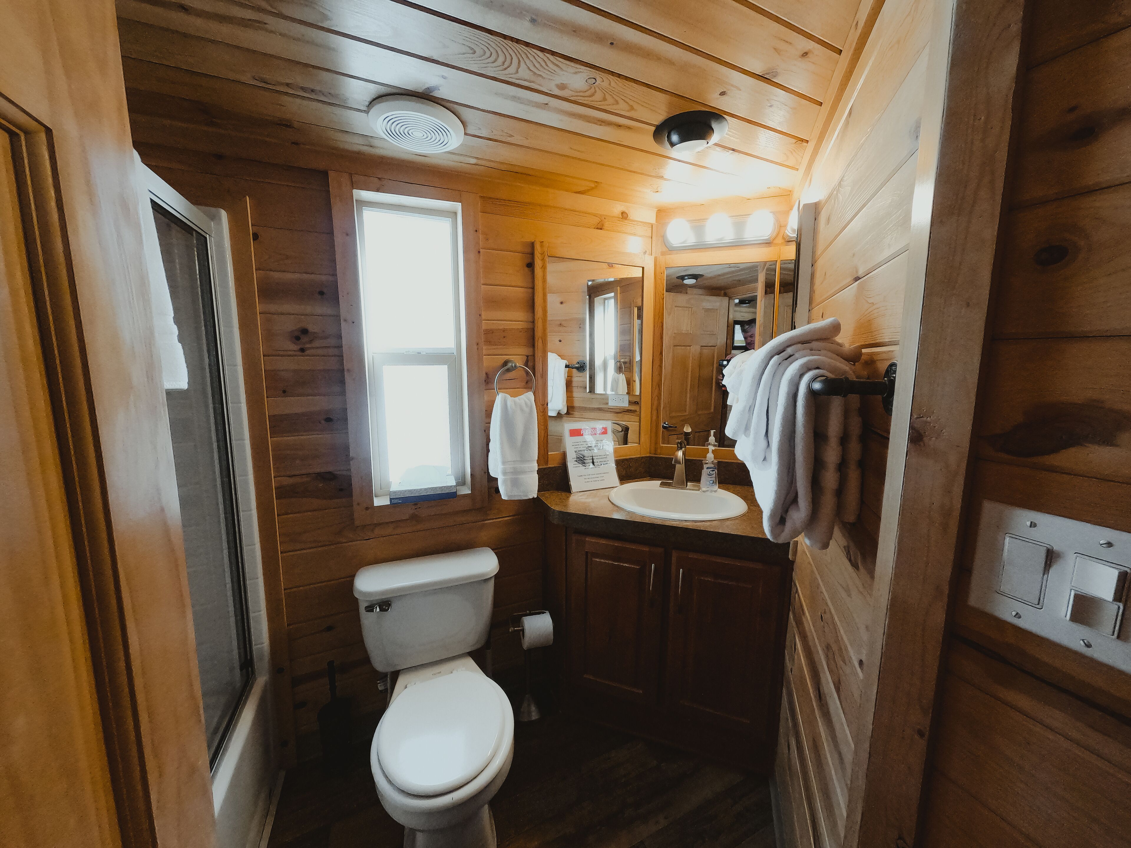 Un baño de cabaña de madera con inodoro, lavamanos y espejo.