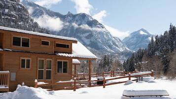Une cabane en bois dotée d’un balcon, entourée de montagnes et d’arbres couverts de neige.