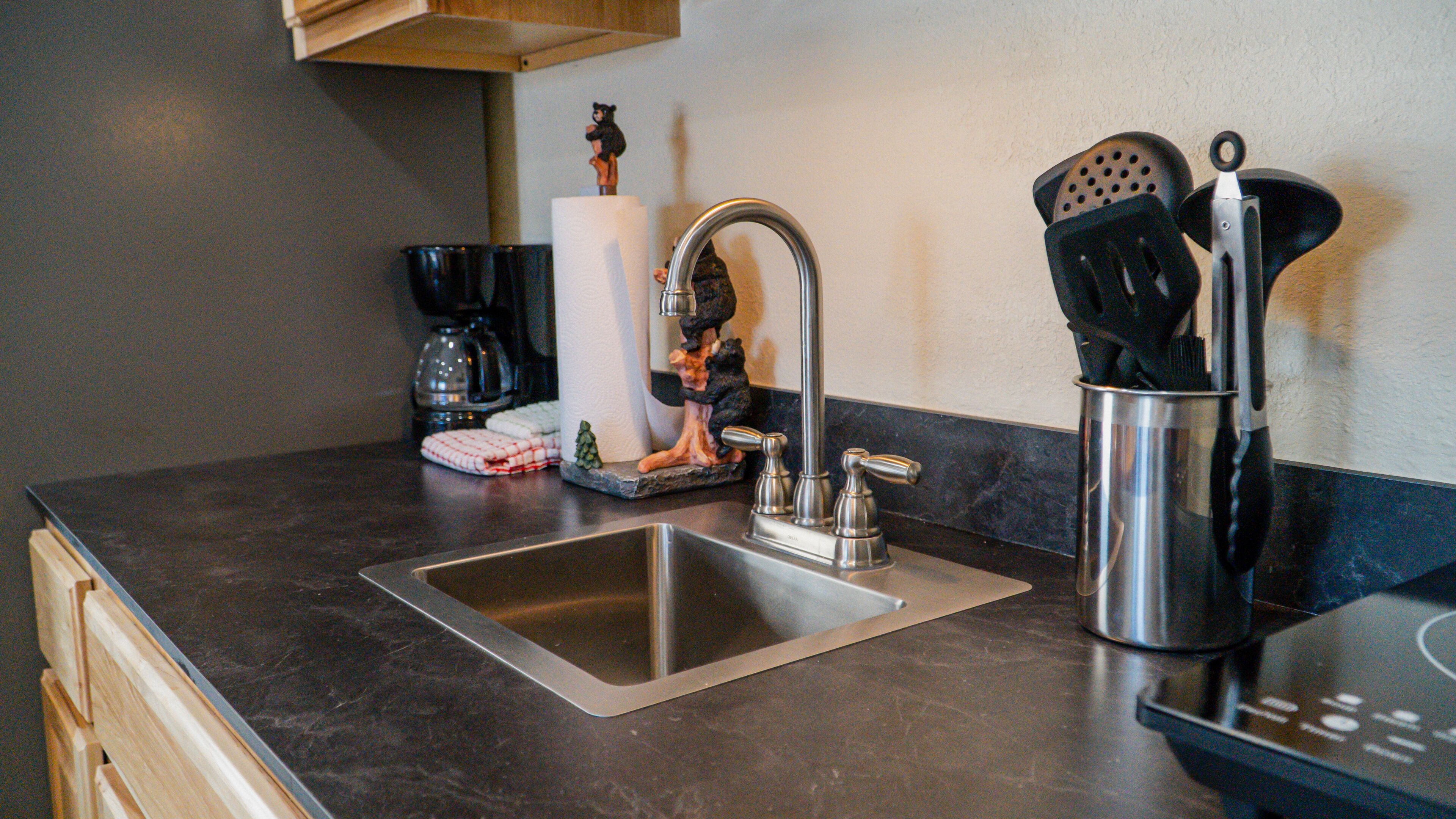 Una cocina con un lavamanos de acero inoxidable, una cafetera y un bloque de cuchillos.