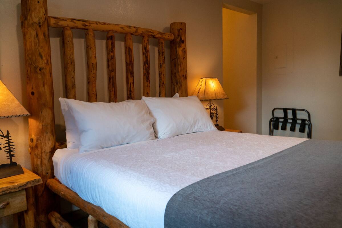 A bed with a wooden headboard, white bedding, and a bedside lamp.