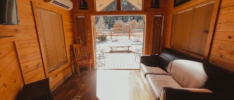 A wooden cabin interior with a sofa, a chair, and a table outside.