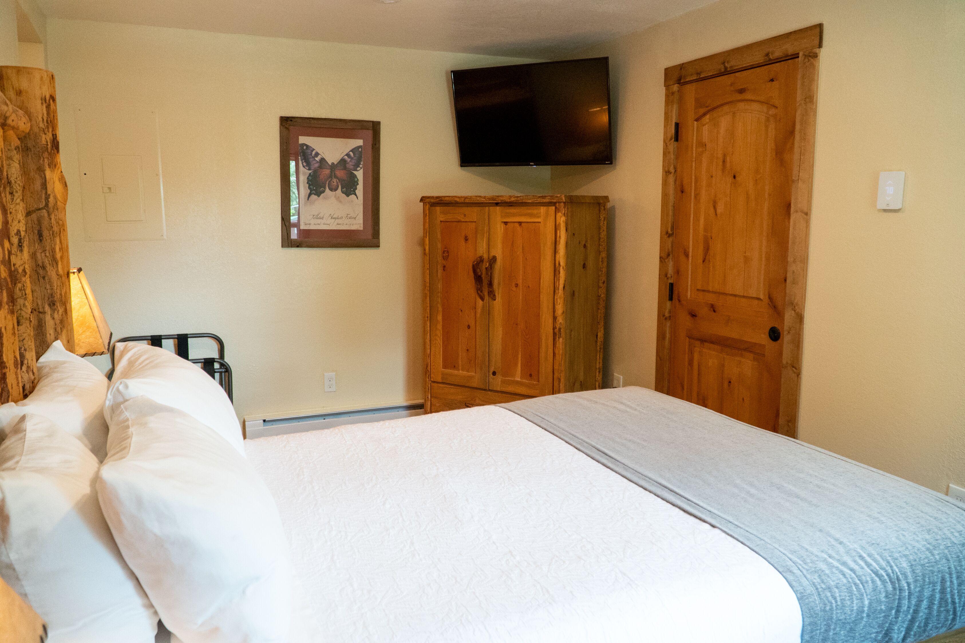 A bedroom with a bed, wooden wardrobe, and a television mounted on the wall.
