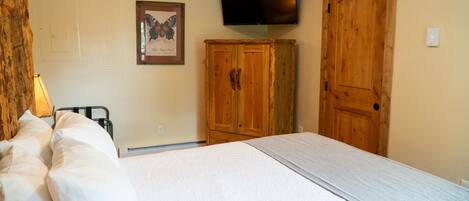 A bedroom with a bed, wooden wardrobe, and a television mounted on the wall.