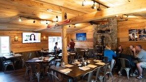 A rustic wooden interior with tables and chairs, a stone fireplace, and a television screen. - Ouray Riverside Resort - Inn & Cabins (Ouray)