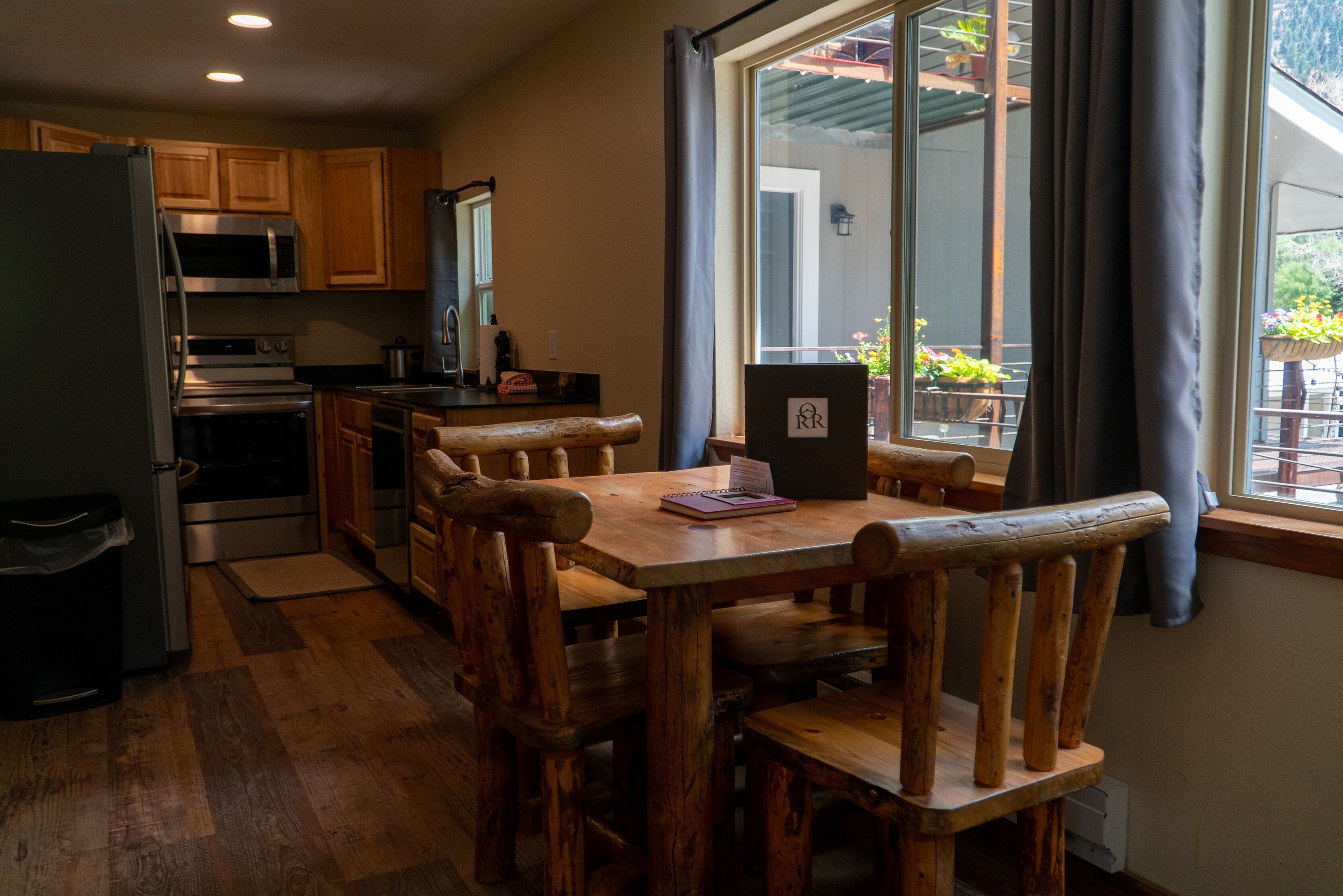 Una cocina con armarios de madera, una mesa de comedor con sillas, un refrigerador y una ventana con cortinas.