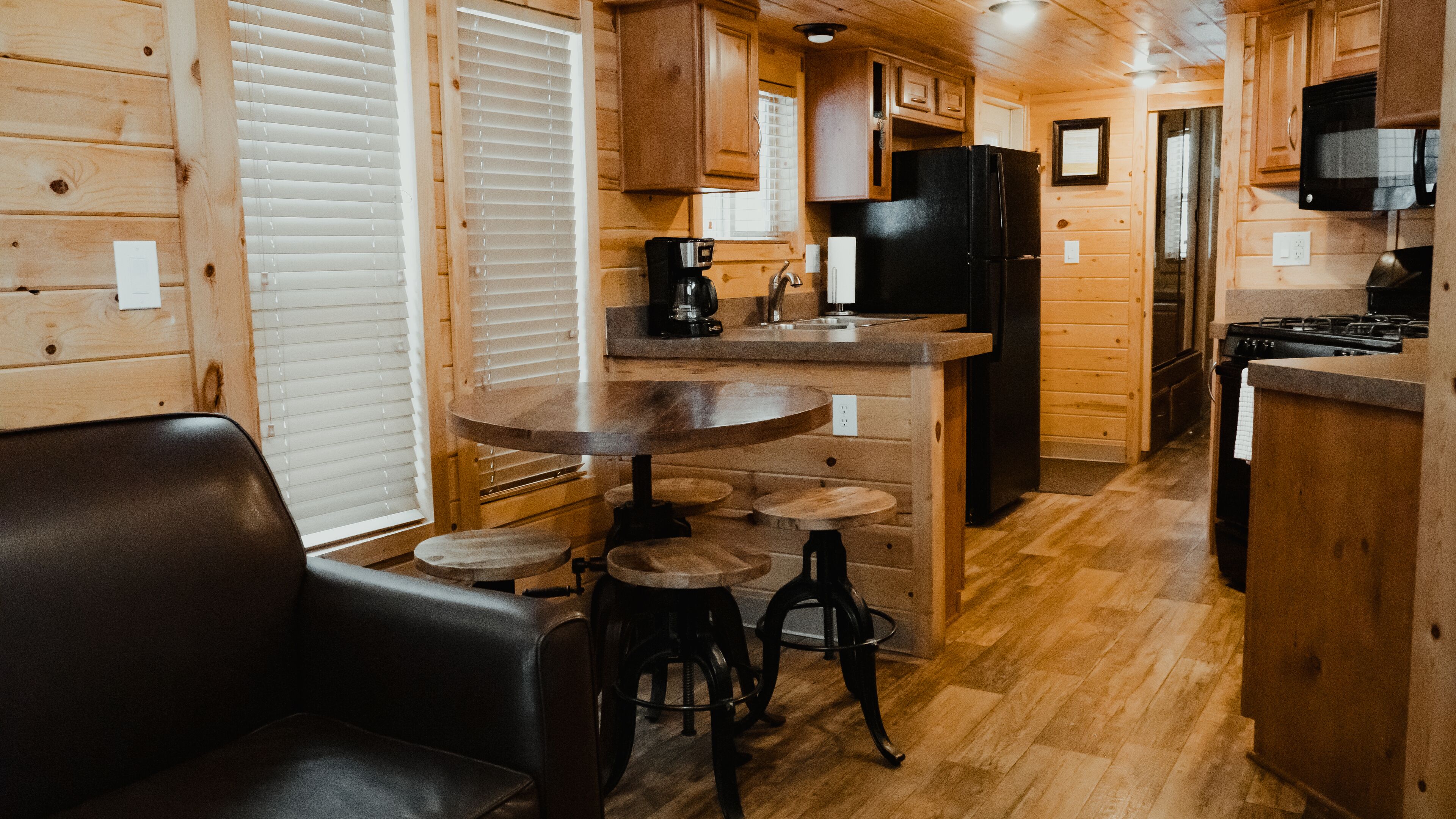 A cozy cabin interior with a wooden dining area, a black refrigerator, and a kitchen with wooden cabinets and a stove.