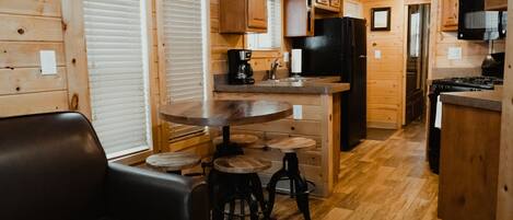 A cozy cabin interior with a wooden dining area, a black refrigerator, and a kitchen with wooden cabinets and a stove.