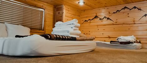 A wooden cabin room with a bed, towels, and a mountain-themed wall.
