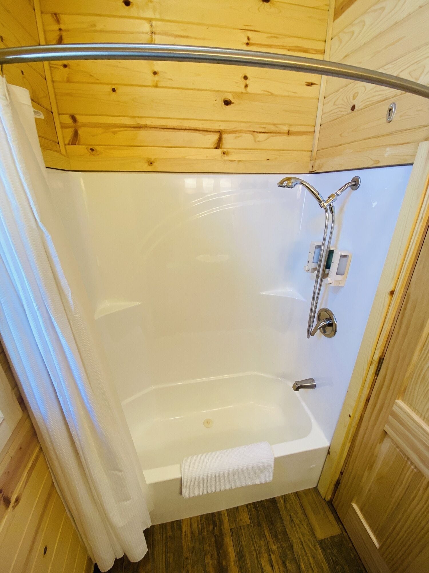 A wooden cabin bathroom with a shower, a bathtub, and a wooden ceiling.