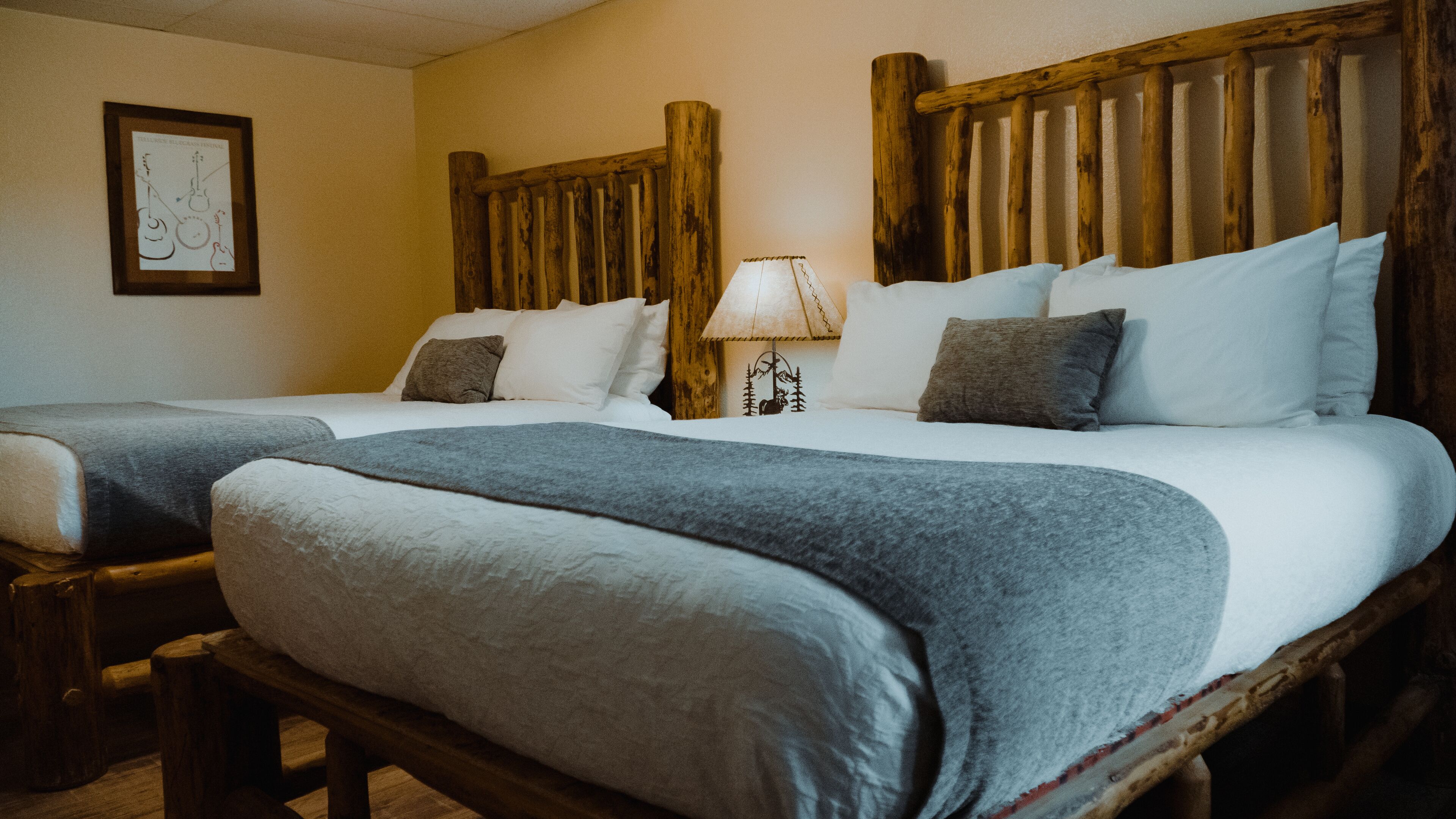 A room with two beds, each with a wooden headboard, white bedding, and a grey throw blanket.