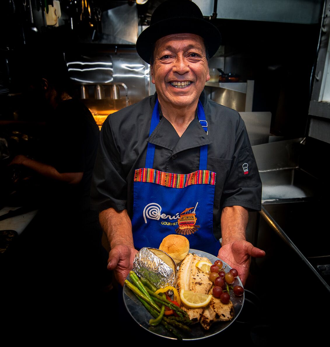 A chef holding a plate of food in a kitchen.