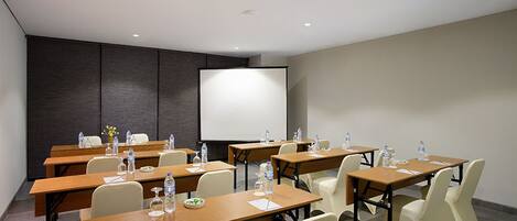 A conference room with multiple tables, chairs, and a large projection screen.