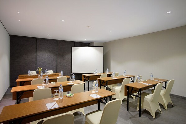 A conference room with multiple tables, chairs, and a large projection screen.