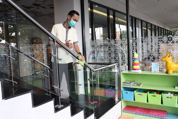 A person descending a glass staircase with metal railings, leading to a green shelf with storage bins and a yellow toy horse.