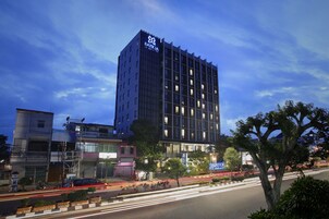 Un hotel moderno con un logotipo destacado, rodeado de infraestructura urbana y una calle concurrida.