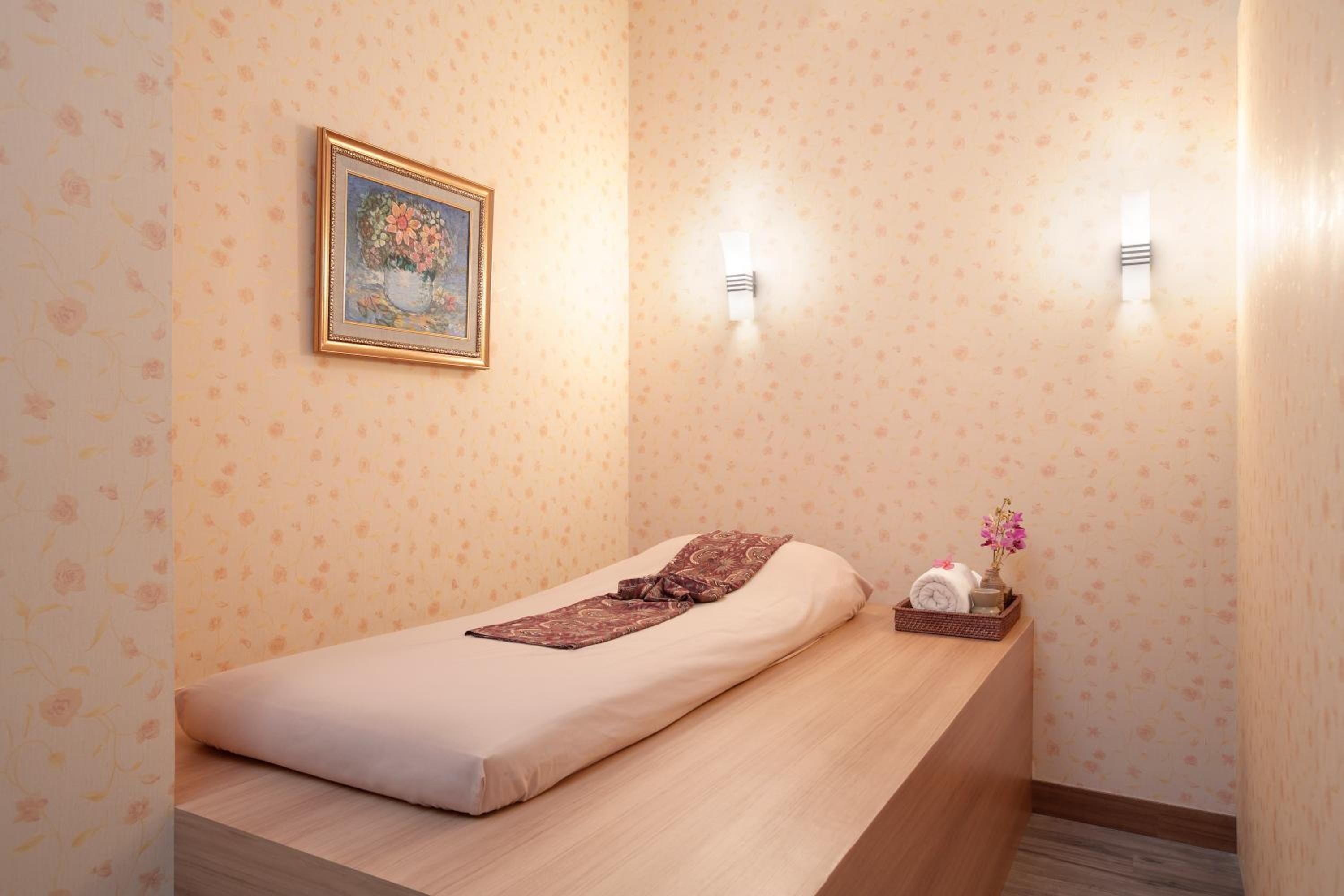 A single bed with a wooden headboard, a small bedside table with a vase of flowers, and a framed picture on the wall.