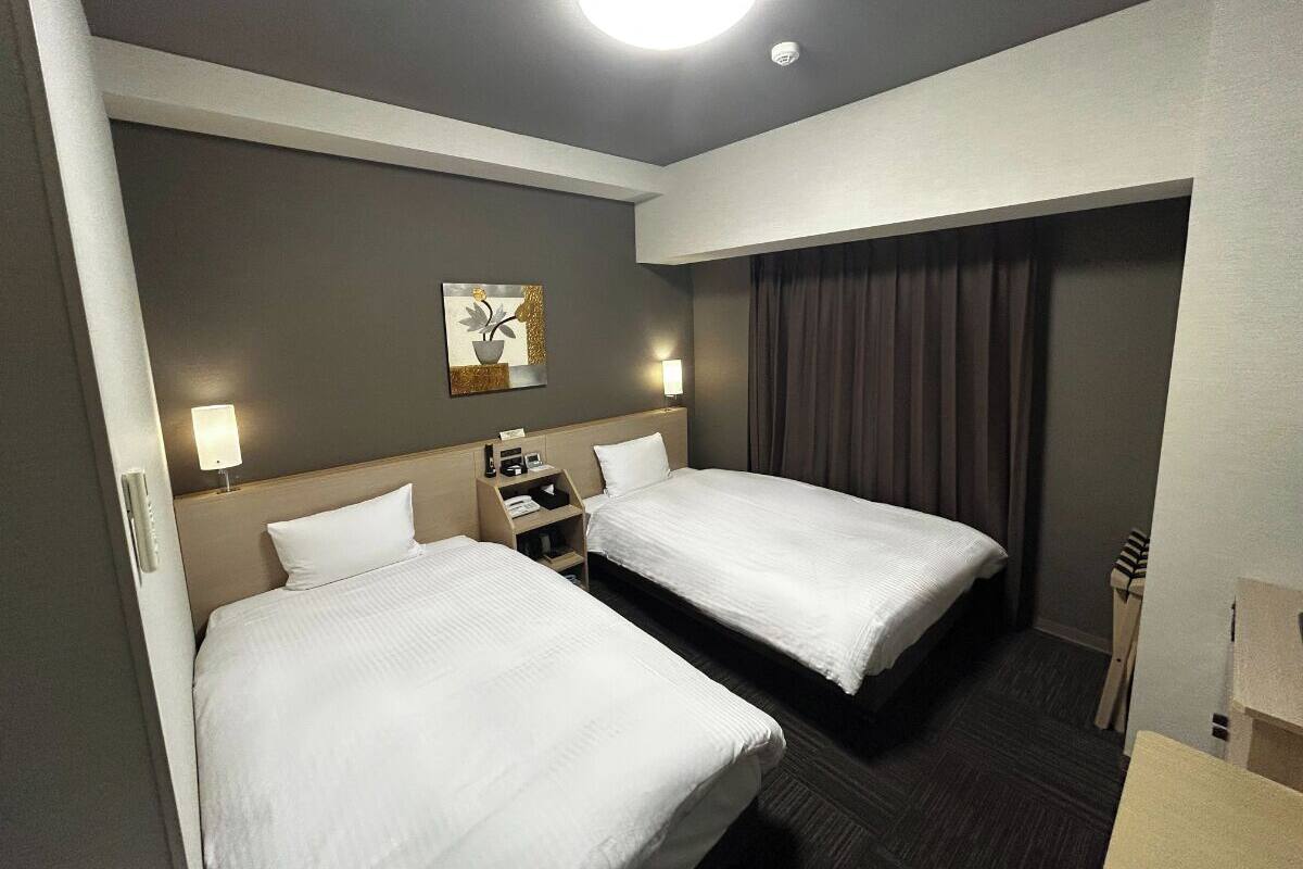 A hotel room with two beds, a nightstand, a lamp, and a painting on the wall.
