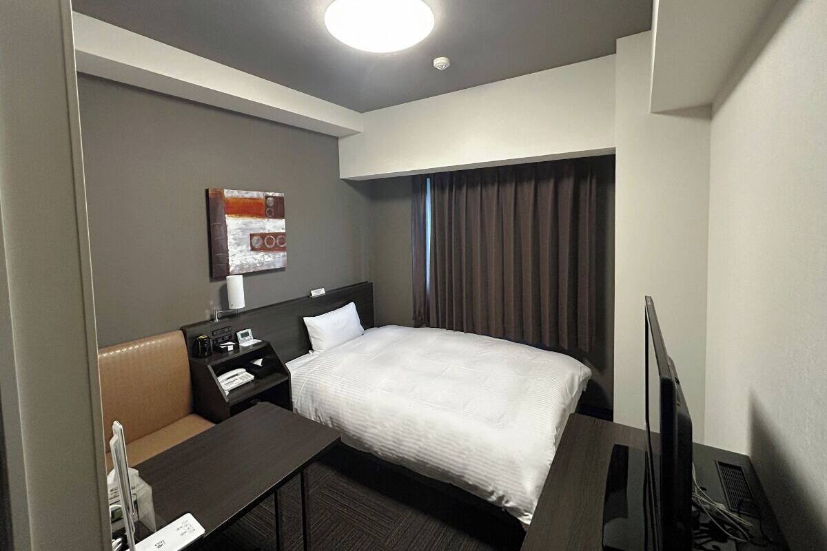 A hotel room with a bed, a desk, a chair, a television, and a window with curtains.