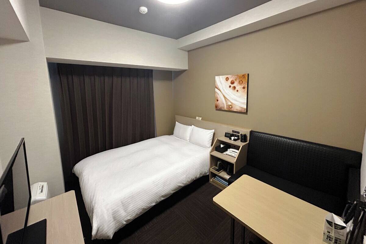 A hotel room with a bed, a desk, a chair, a TV, a wardrobe, and a painting on the wall.