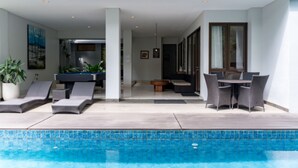 Zona junto a la piscina con sillones de descanso, una mesa de comedor y una planta en maceta.