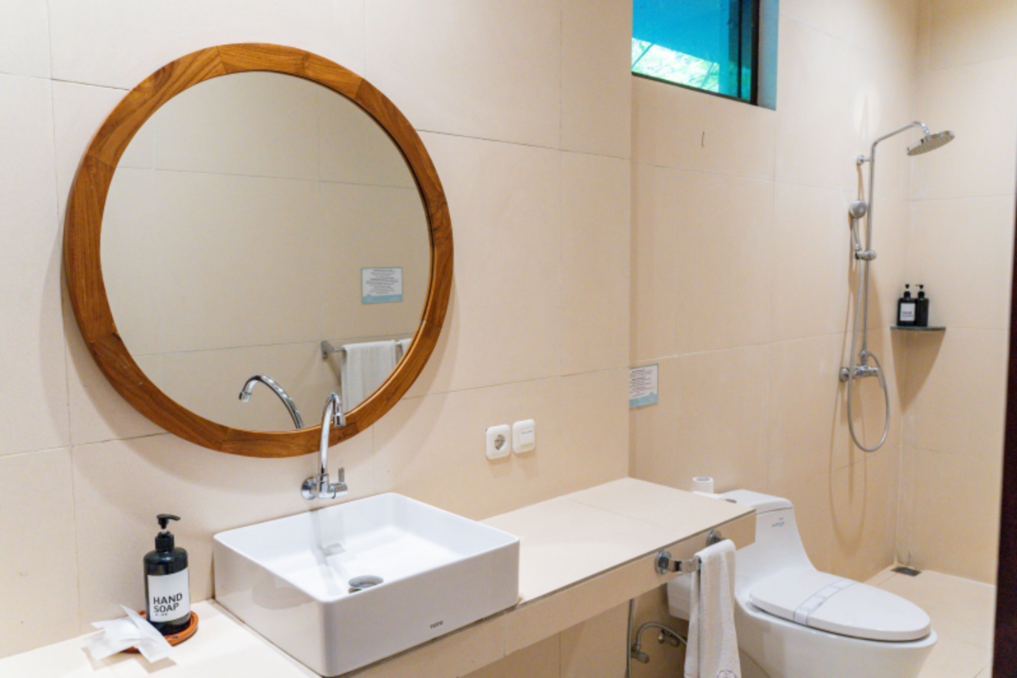 A bathroom with a round mirror, a sink, a toilet, and a shower.