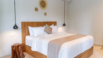 A bedroom with a wooden headboard, white bedding, a wooden stool, and a wall-mounted air conditioner.