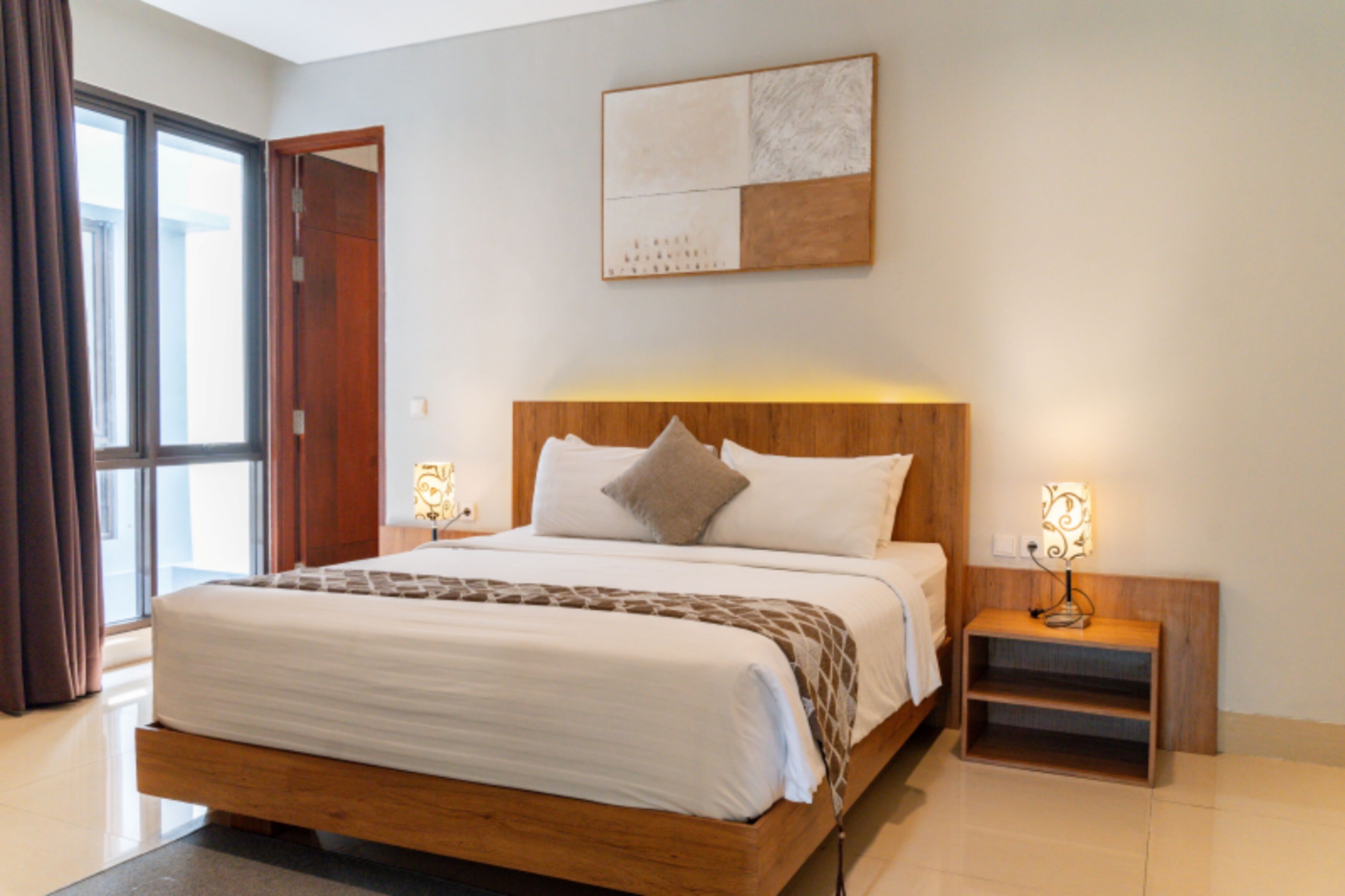 Un dormitorio con una cama grande, mesitas de noche, un cabecero de madera, una ventana con cortinas y una obra de arte colgada en la pared.