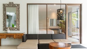 Una sala moderna con un conjunto de sofá, una mesa de centro de madera, un espejo decorativo y un ventanal corredero que da a un balcón.