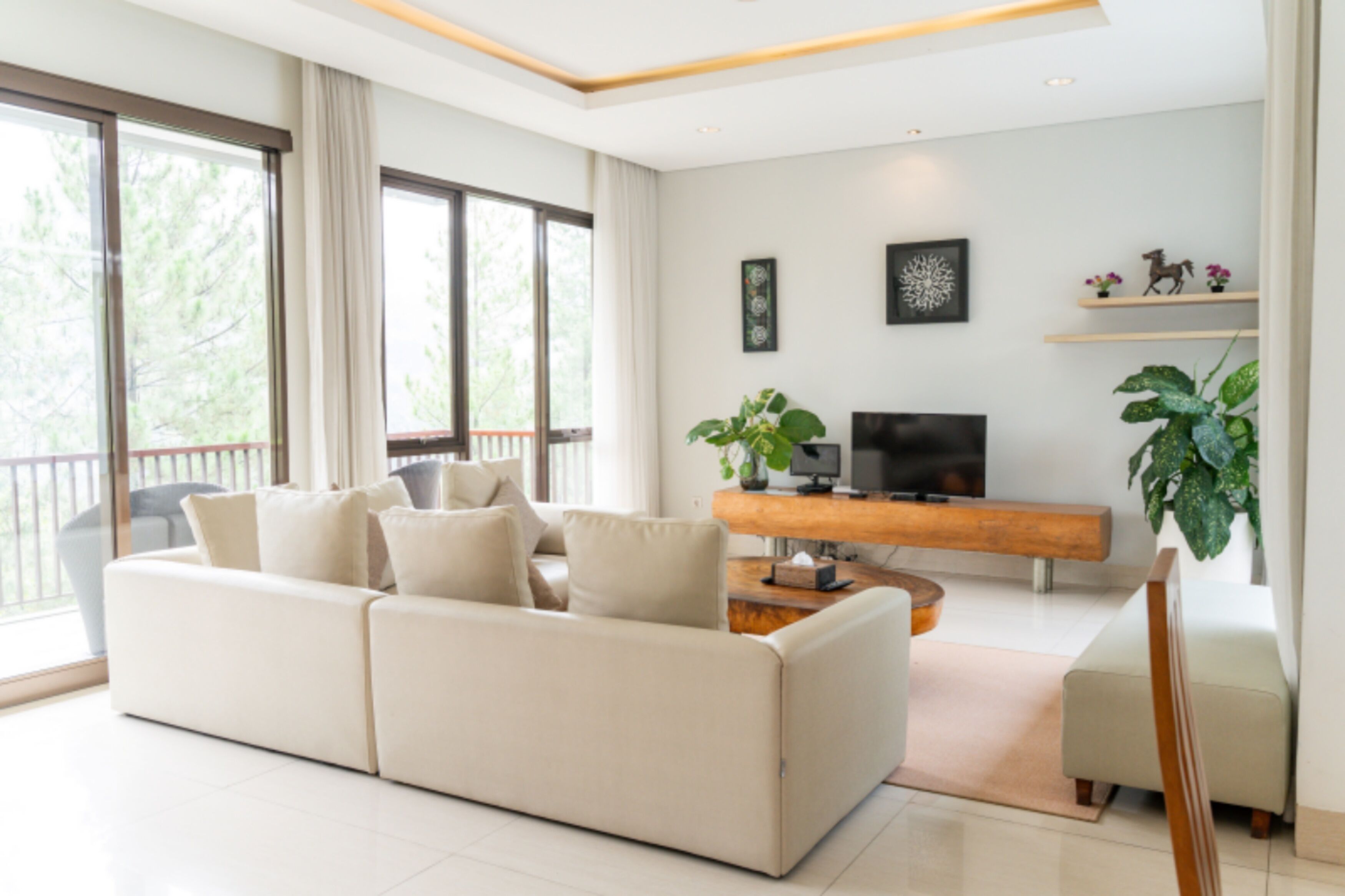 Un salon moderne avec un canapé d’angle, un téléviseur à écran plat, un buffet en bois et de grandes fenêtres.