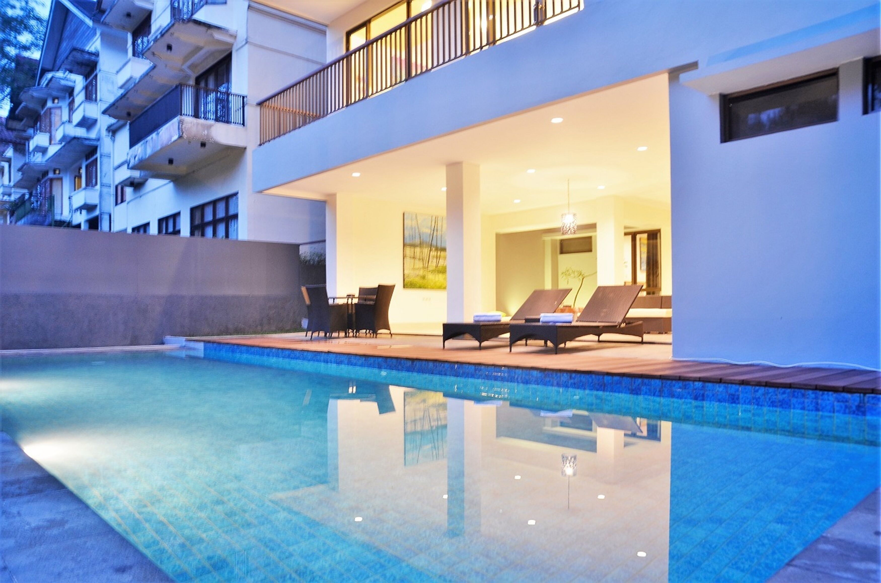 A modern hotel with a swimming pool, lounge chairs, and a balcony overlooking the pool.