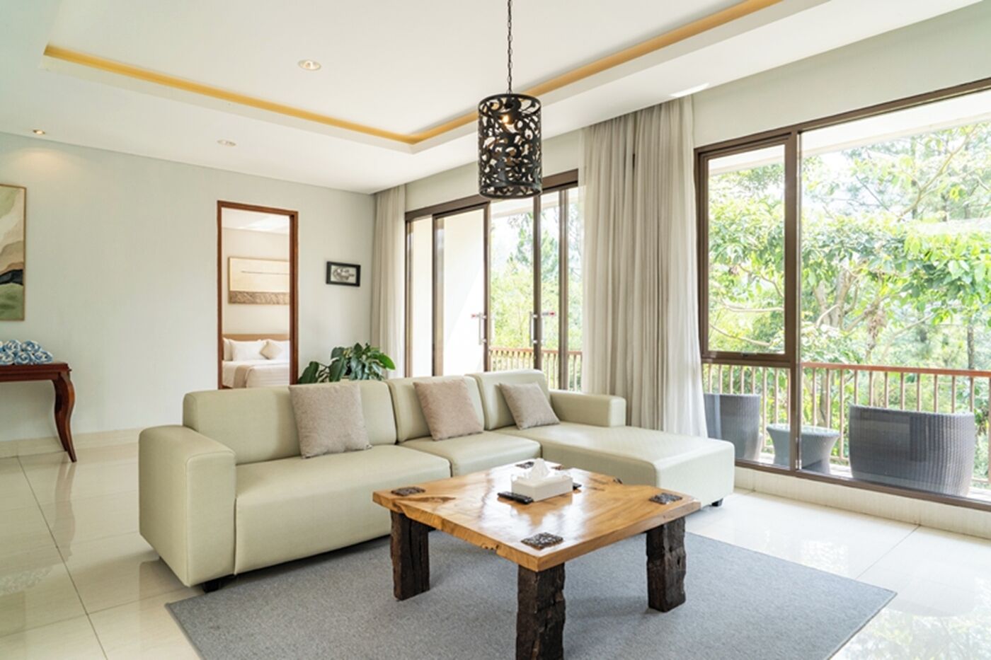Un salon moderne avec un canapé, une table basse et de grandes fenêtres donnant sur un paysage verdoyant.