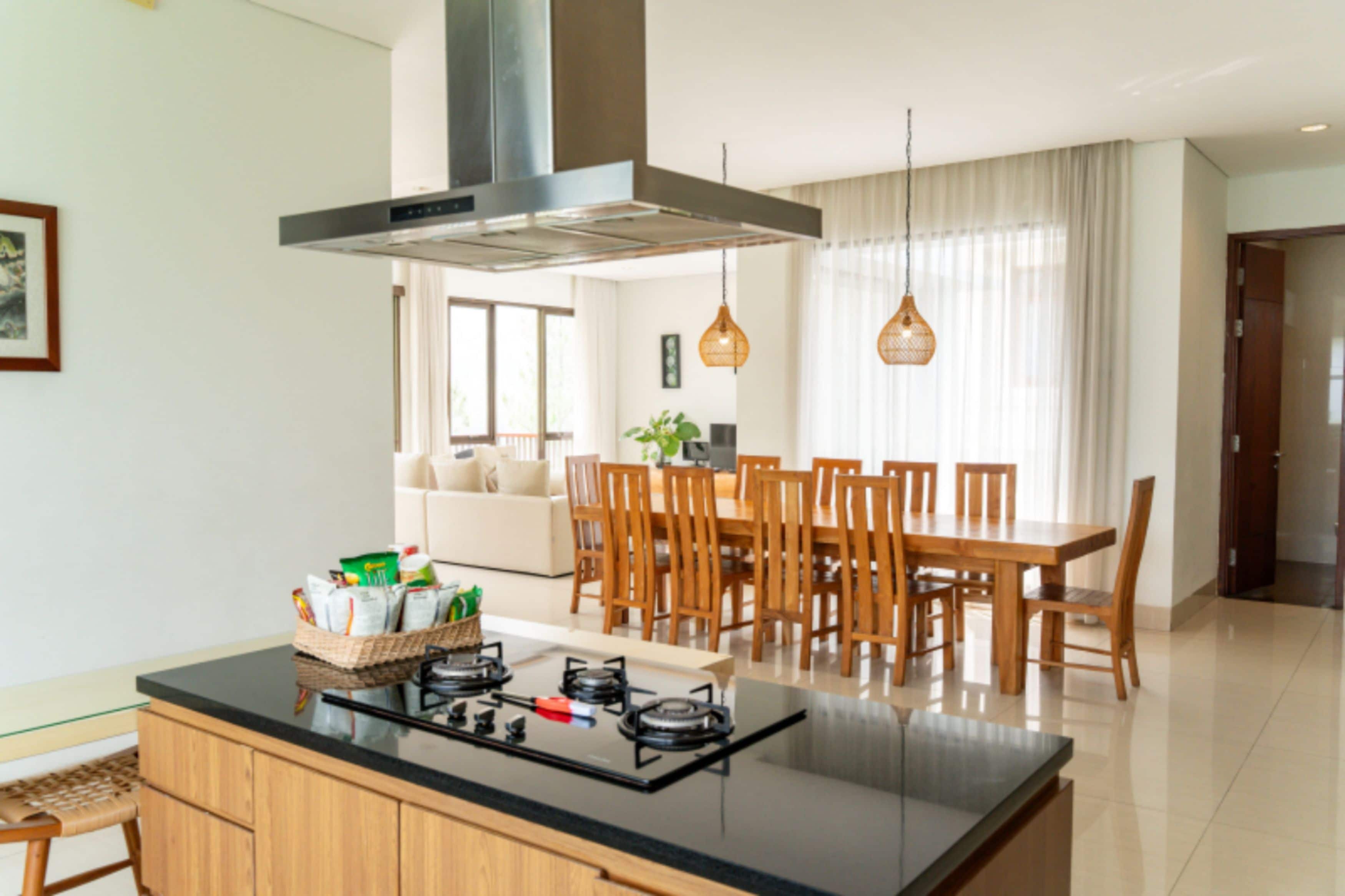 Una cocina moderna con una isla central, comedor con sillas de madera y un amplio ventanal con cortinas.