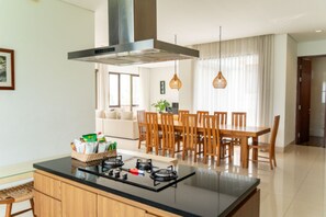 A modern kitchen with a central island, dining area with wooden chairs, and a large window with curtains. - Hikari Hill View 7BR Villa with a Private Pool (Cimenyan)