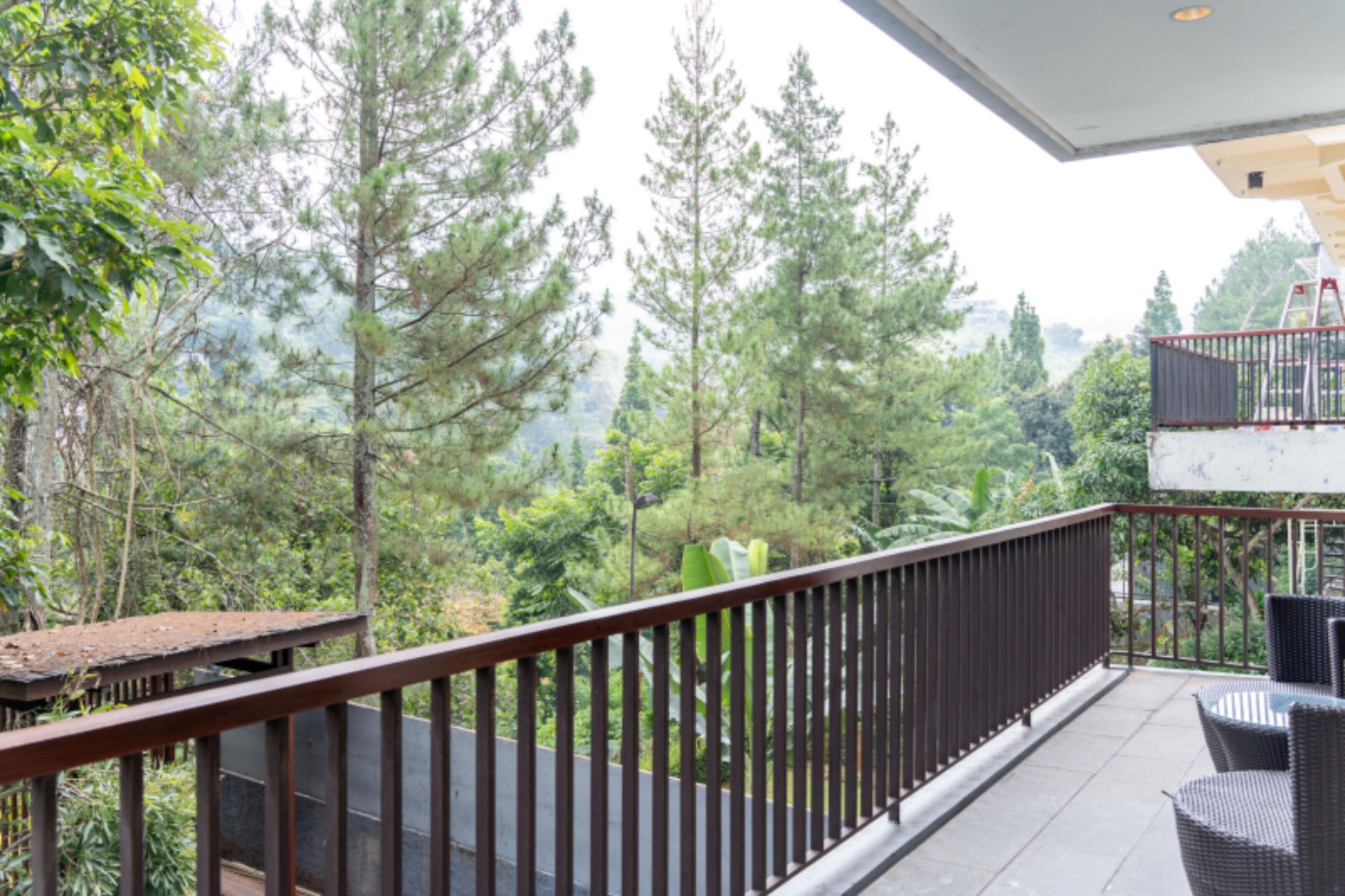 A balcony with a view of a forested area, a railing, and outdoor furniture.