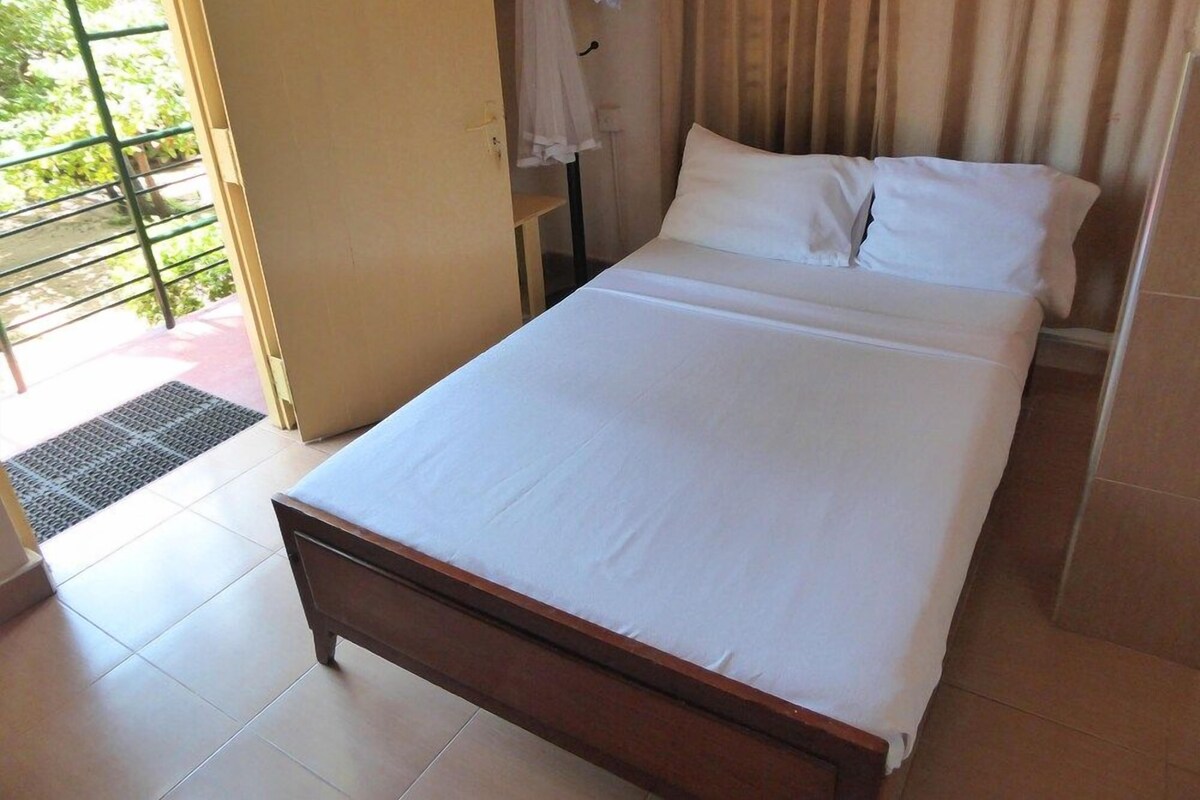 A single bed with white bedding in a room with a tiled floor and a door leading outside.