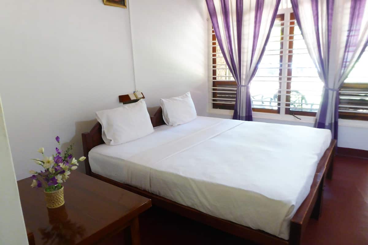 A neatly made bed with white linens, a wooden headboard, and a small bedside table with a vase of flowers.