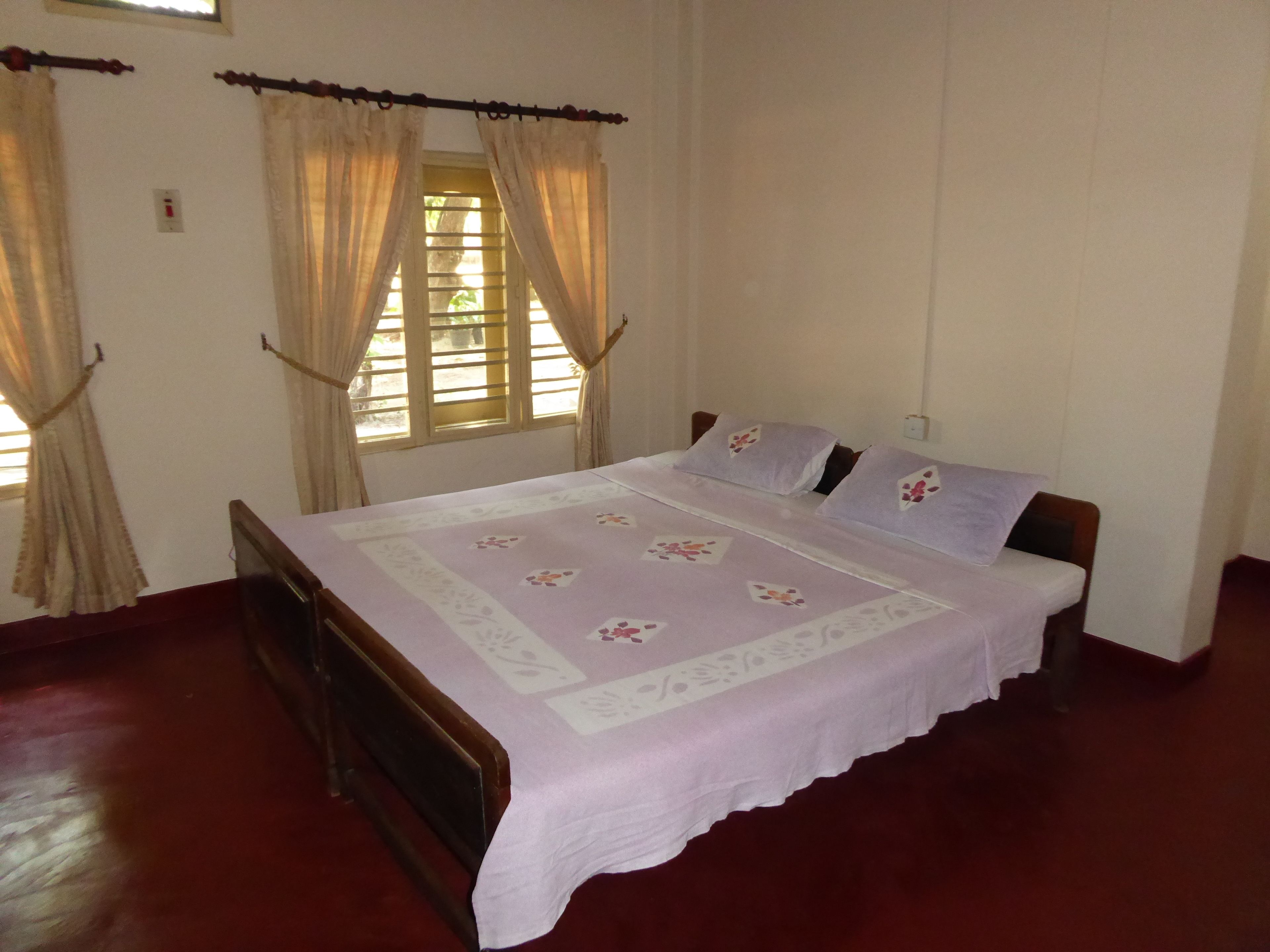 A bedroom with a wooden bed, a window with curtains, and a red floor.