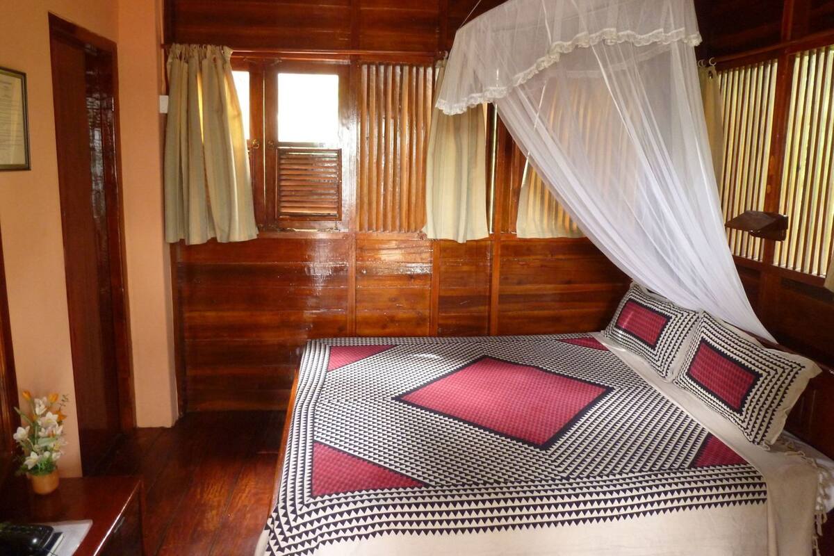 A wooden room with a bed, curtains, and a window.