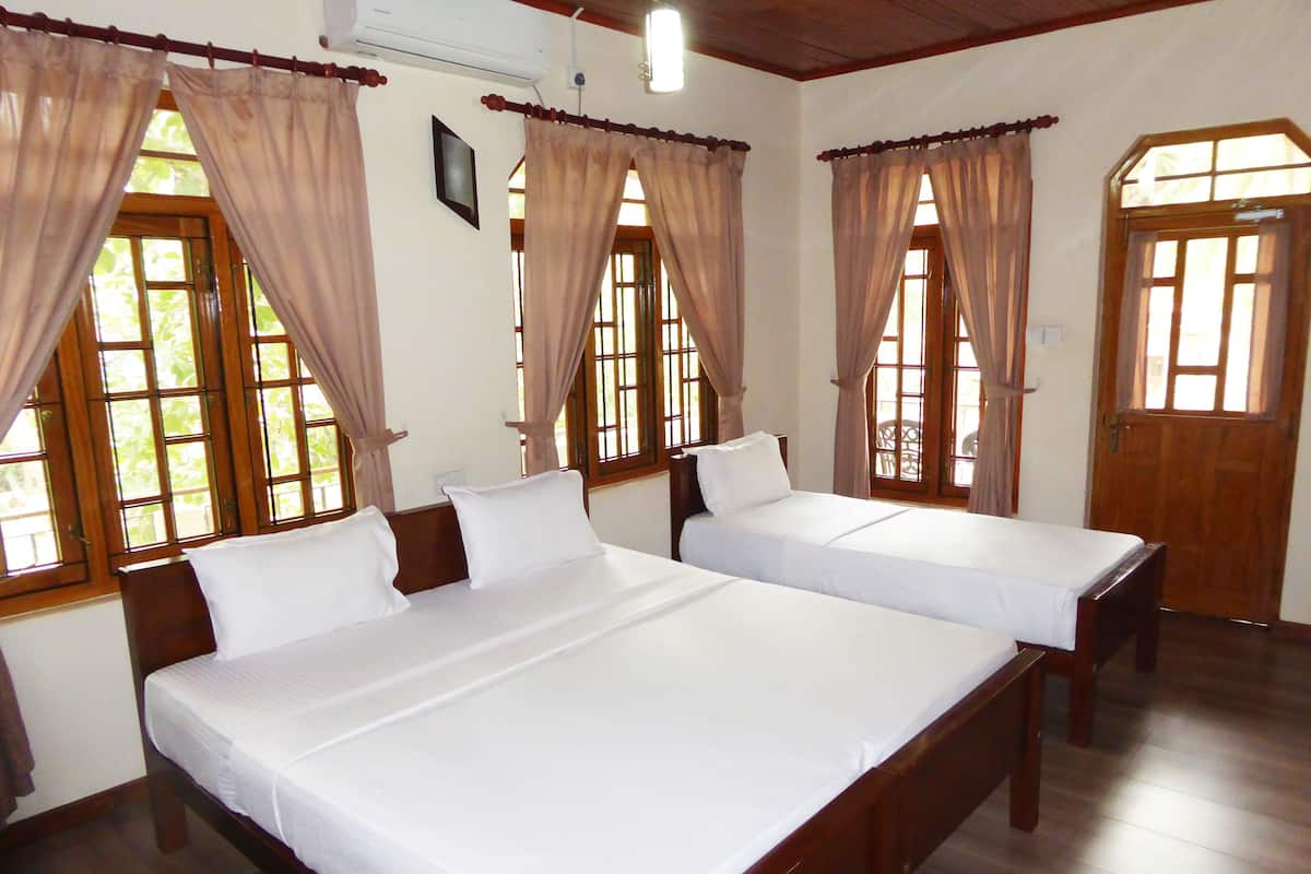 A hotel room with two beds, wooden floors, and large windows with curtains.