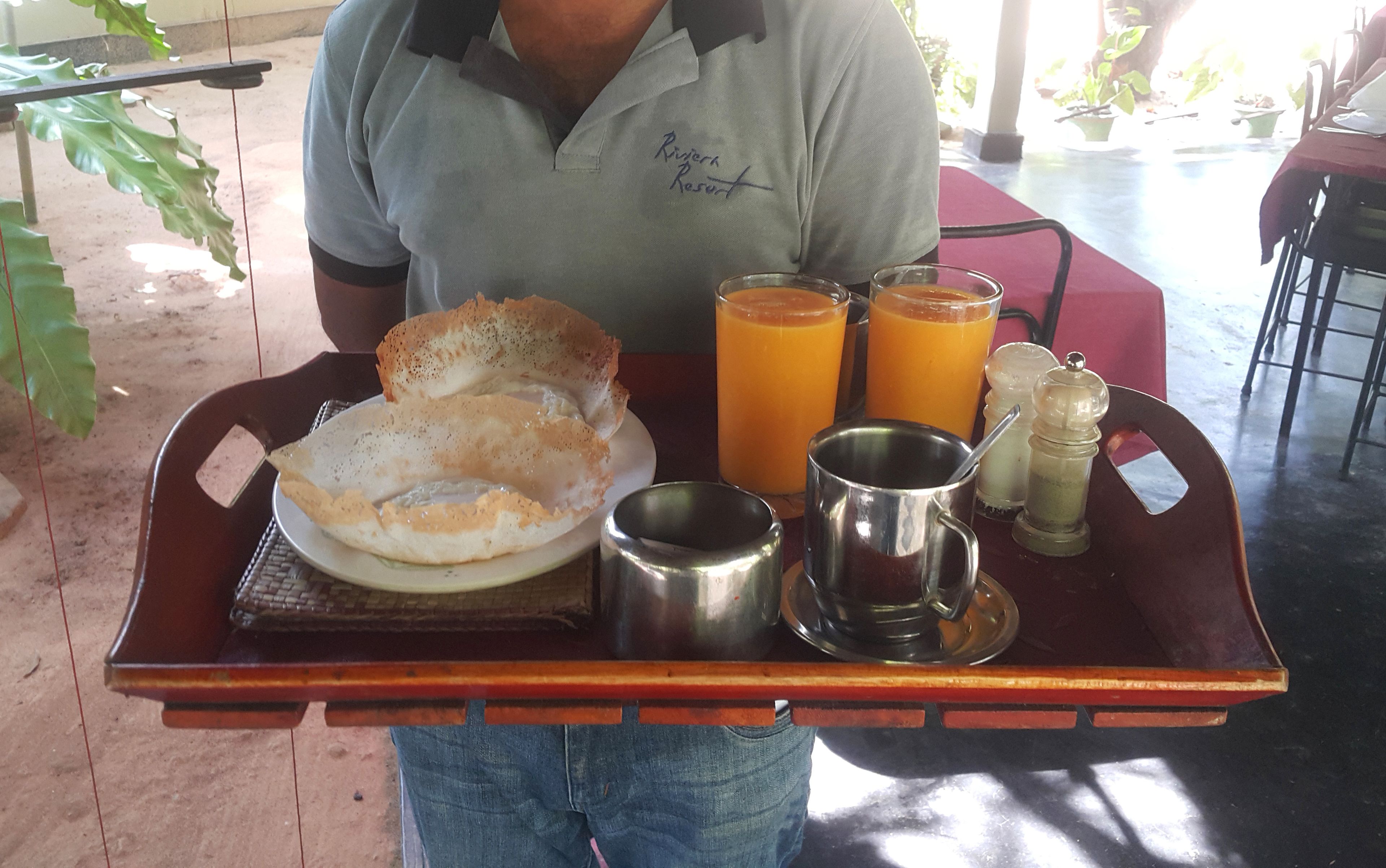 A tray with breakfast items including crepes, two glasses of orange juice, a metal cup, and salt and pepper shakers.