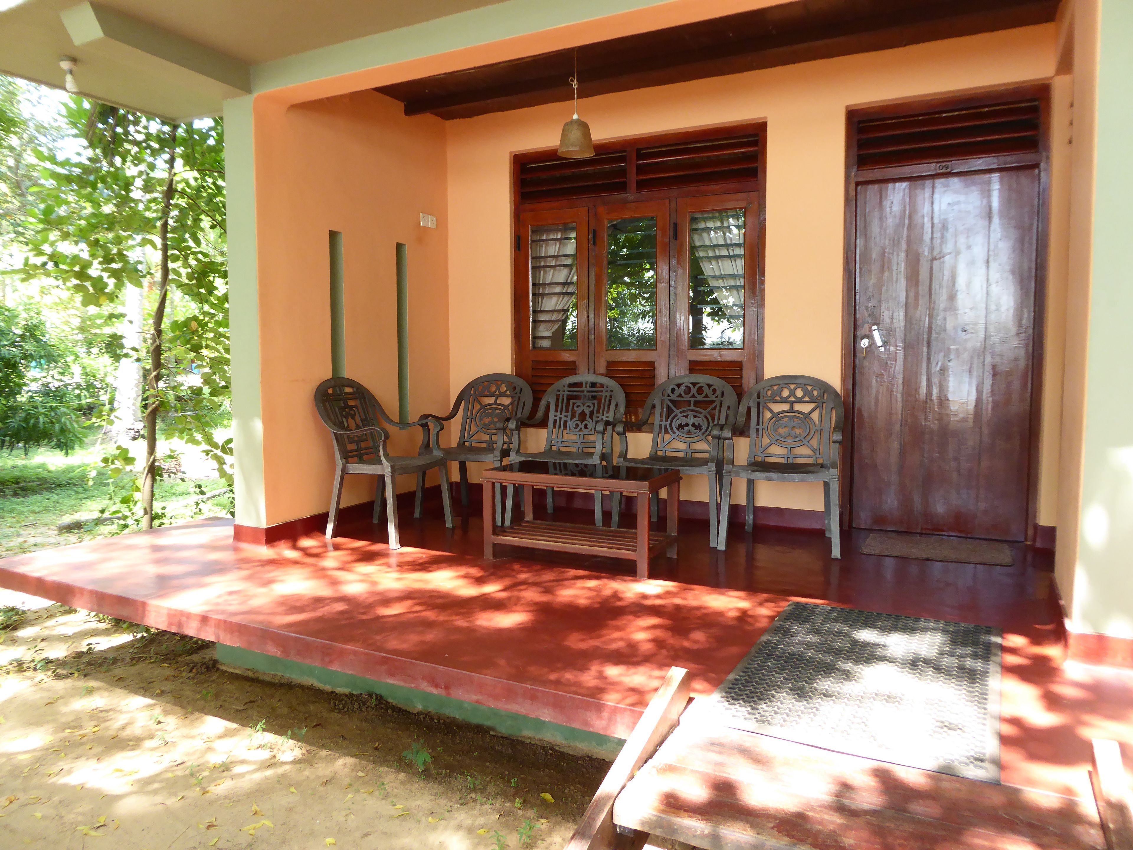 A covered porch with a table and chairs, a wooden door, and a window with shutters.