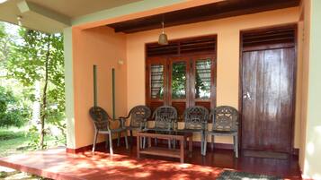 A covered porch with a table and chairs, a wooden door, and a window with shutters.
