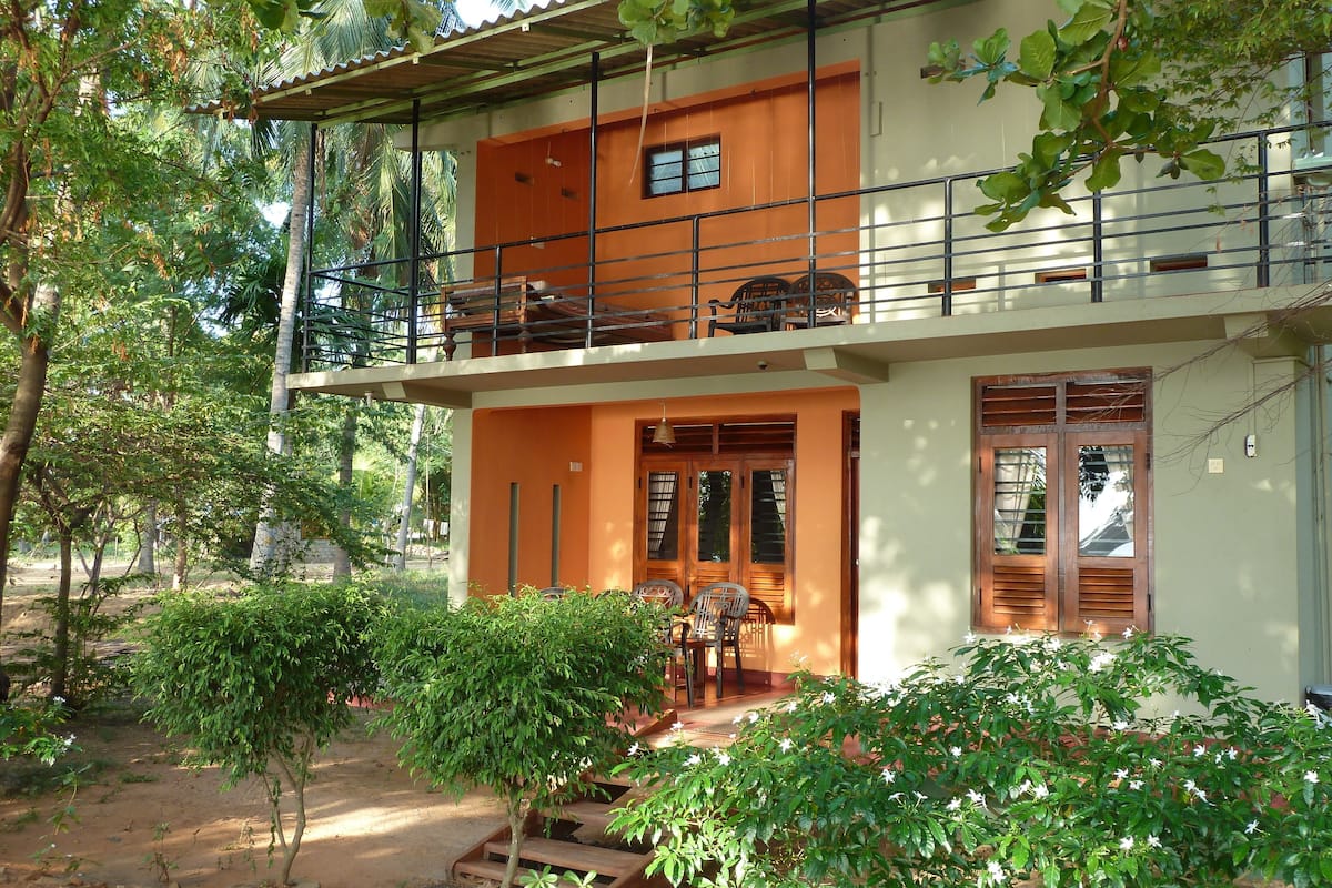 A two-story building with a balcony, wooden doors, and a small garden area with steps leading to the entrance.