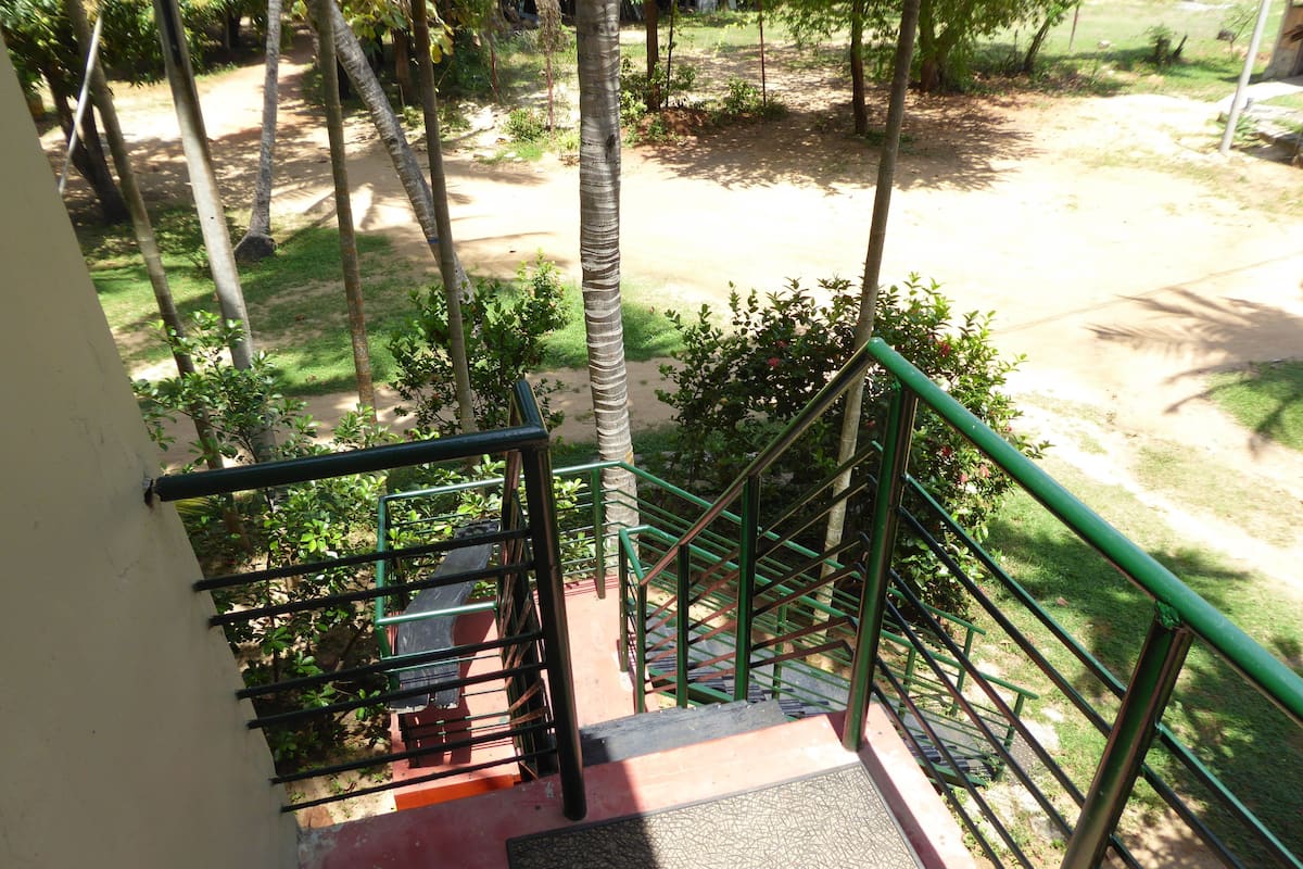 A staircase with green railings leading to a covered outdoor area with trees and a dirt path.